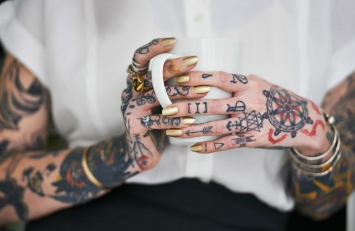 Viele farbige Tattoos an Fingern und Armen, goldener Nagellack, goldener massiver Schmuck 