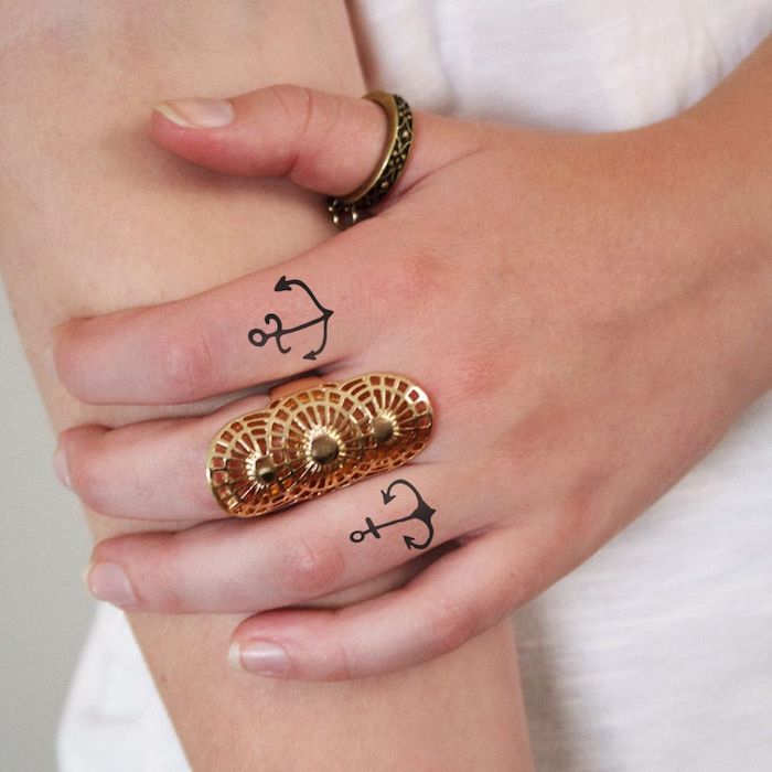 Anker Tattoos am Zeigefiner und am Ringfinger, massive goldene Ringe am Mittelfinger und am Daumen 