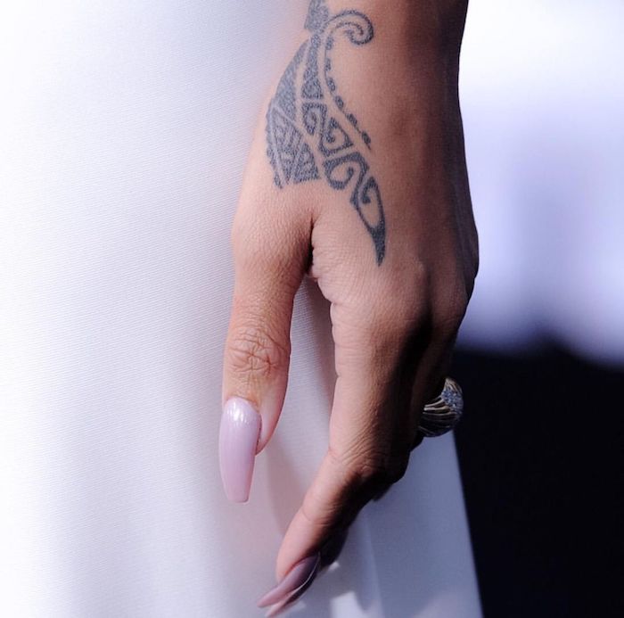 Kleines Tattoo an der Hand, Nagellack in Pastellfarbe, ovale Nägel, massiver goldener Ring 