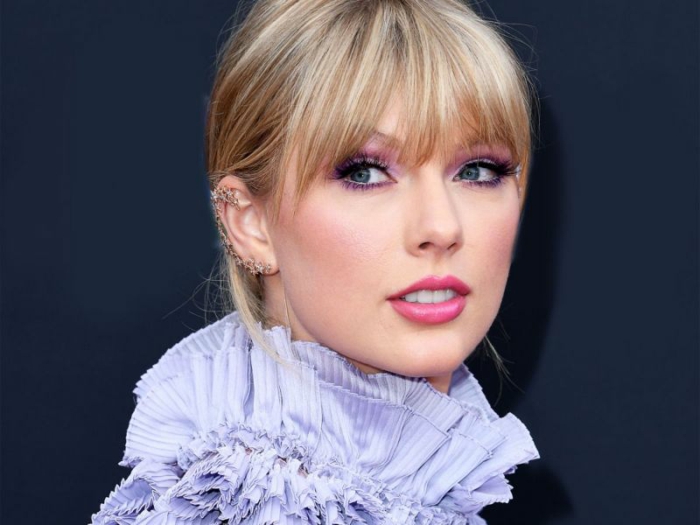 Taylor Swift mit einem blauen Kragen, rosa Lippenstift, Hochsteckfrisur mit Pony