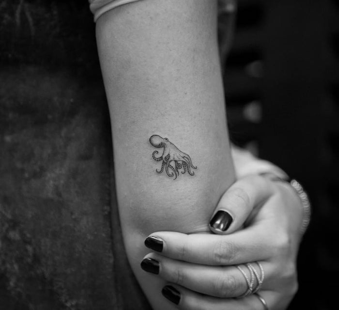 Mini Kraken Tattoo am Oberarm, kleine Arm Tattoos, schwarzer Nagellack, silberne Ringe 