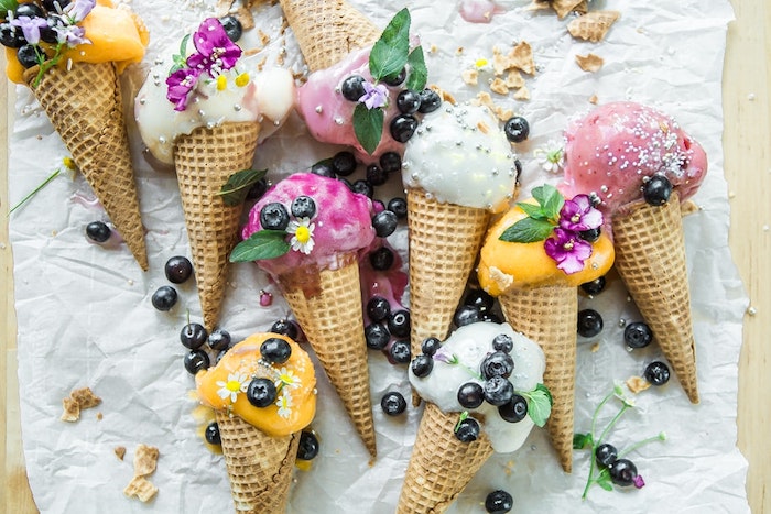 Eis garniert mit frischen Heidelbeeren, Blüten und Zuckerperlen, Fruchteis und Vanilleeis in Waffeln 
