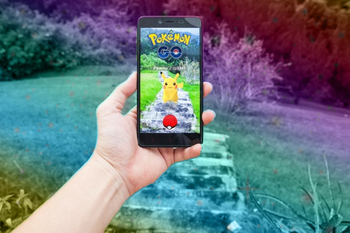 Pokemon Go, ein Pickachu auf einer Wiese, ein Spieler trägt ein Handy und fängt ihn