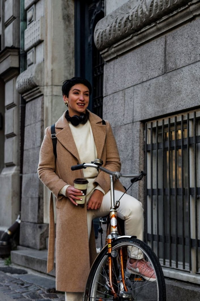 kataloge damenmode, eine junge und stilvolle frau mit fahrrad und weißen outfit und beigem mantel