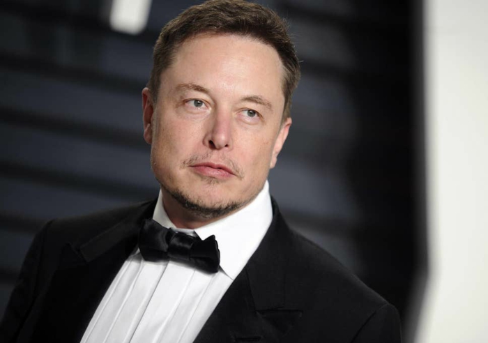 Elon Musk ist zufrieden, weil die Tesla Aktien steigen, hier ist er mit schwarzem Anzug