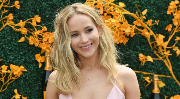 Jennifer Lawrence auf Hintergrund stehen gelbe Blumen, sie hat blonde Haare