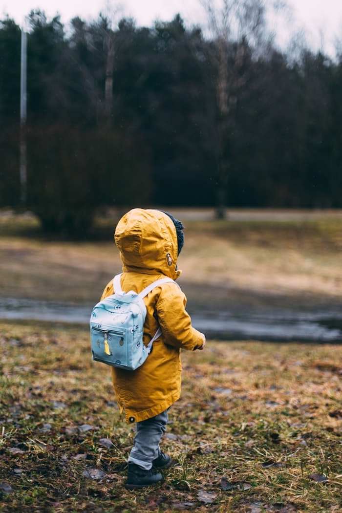 Süßes Kind mit gelber Regenjacke und blauem Rucksack 