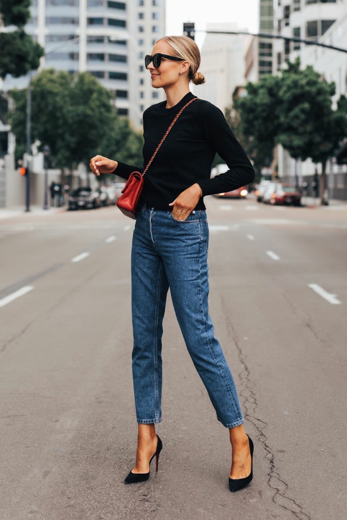 Dame in Jeans, schwarze High Heels, rote Tasche aus Leder und schwarze Bluse, sportlich elegante outfits damen