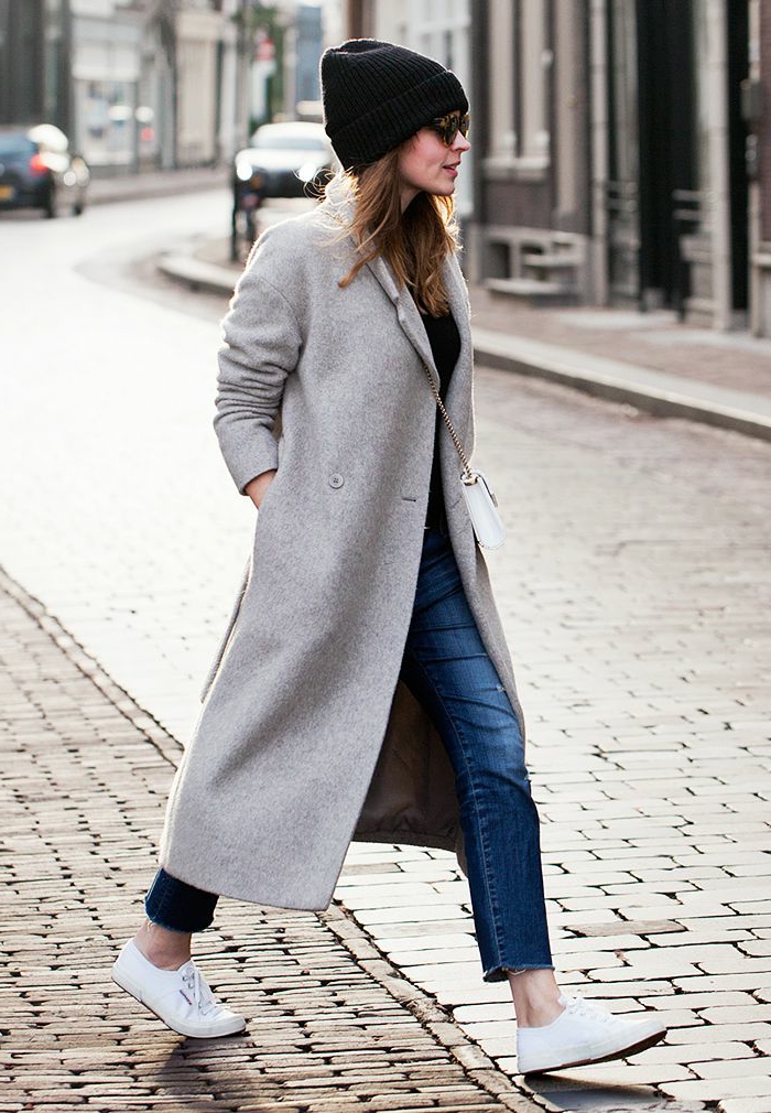 Dame im grauen Mantel, gepaart mit Jeans, weiße Sneakers und schwarze Mütze