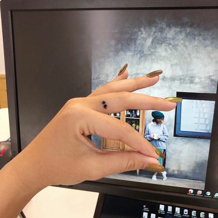 Kleines semicolon tattoo am Mittelfinger, was bedeutet ein semikolon, Hand mit goldenem Nagellack 