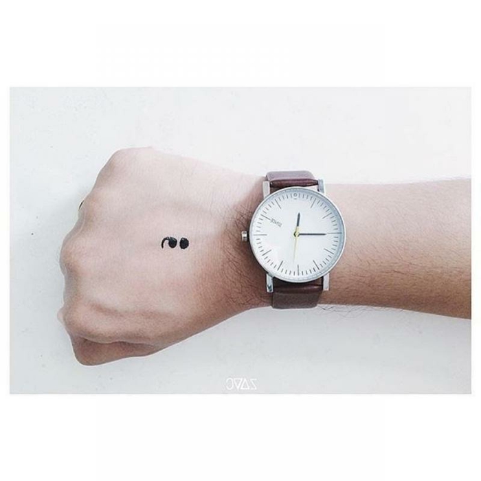 Bild von einer Hand mit einem Semicolon Tattoo und eine Uhr, geballte Hand, was bedeutet ein semikolon