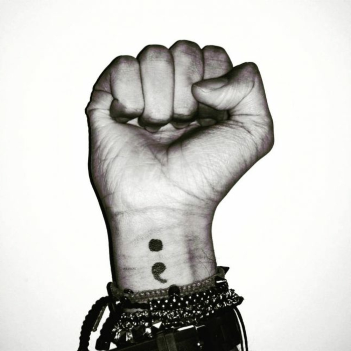 Zusammengeballte Hand mit einem Semicolon Tattoo am Arm, was bedeutet ein semikolon, viele Armbänder