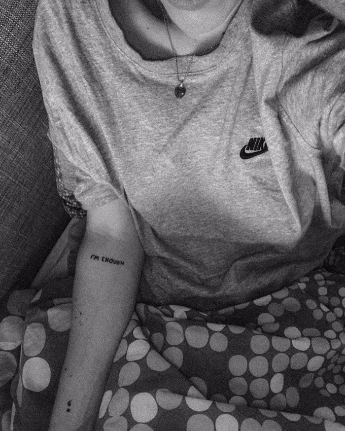 Schwarz-weißes photo von einer Frau mit einem Semicolon und I'm Enough Tattoo am Arm, was bedeutet ein semikolon