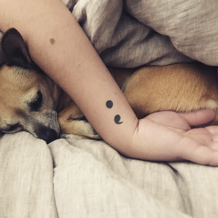 Hand mit einem Semicolon Tattoo und ein eingekuschelter Hund, zeichen für depression