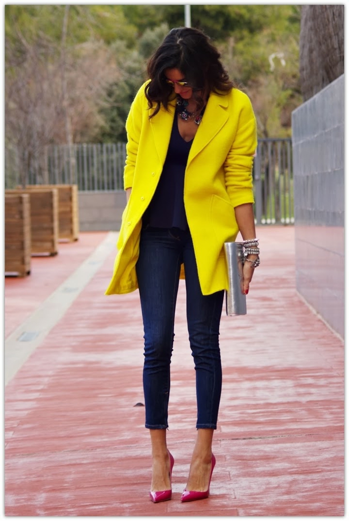 Große, dunkelhaarige Dame in Jeans, gelber Mantel, pinke Pumps, trägt ein Clutch