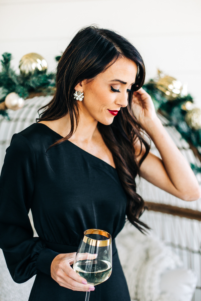 Schwarzes Cocktail Kleid mit einem Ärmel, offene gewellte Haare, seitlich getragen, silberne Ohrringe mit Kristallen 