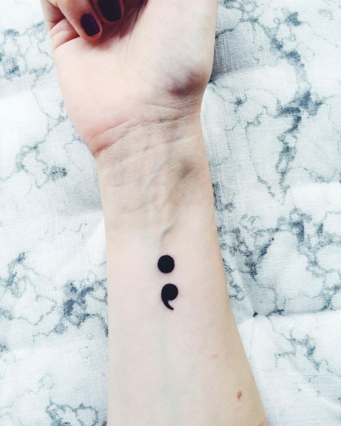 Hand mit schwarzem Nagellack, schwarzes Tattoo von einem Semikolon am Arm, was bedeutet ein semikolon
