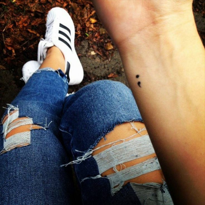 Dezentes Semicolon Tattoo auf einer Hand. project semicolon, zerrissene Jeans, weiße sneakers