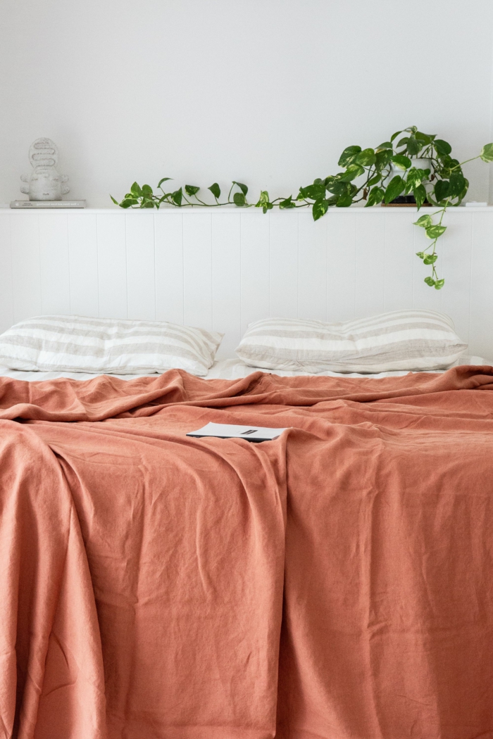 Großes Bett mit Bettwäsche in altrosa Farbe, zwei weiße gestreifte Kissen, Aktuelle Wohnraum Farben, Grüne Pflanze im Hintergrund
