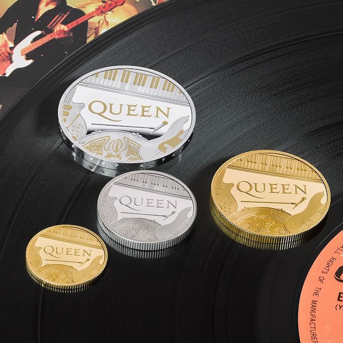vier kleine und große münzen mit dem logo von der britischen band queen, ein Mikrofon und ywei gitarren und ein fl[gel 