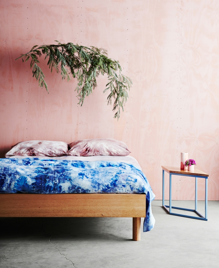 Schlafzimmer rosa grau, großes Bett mit blauen Bettwäschen, Kissen in pink, grüne Pflanze, rechteckiger Tisch