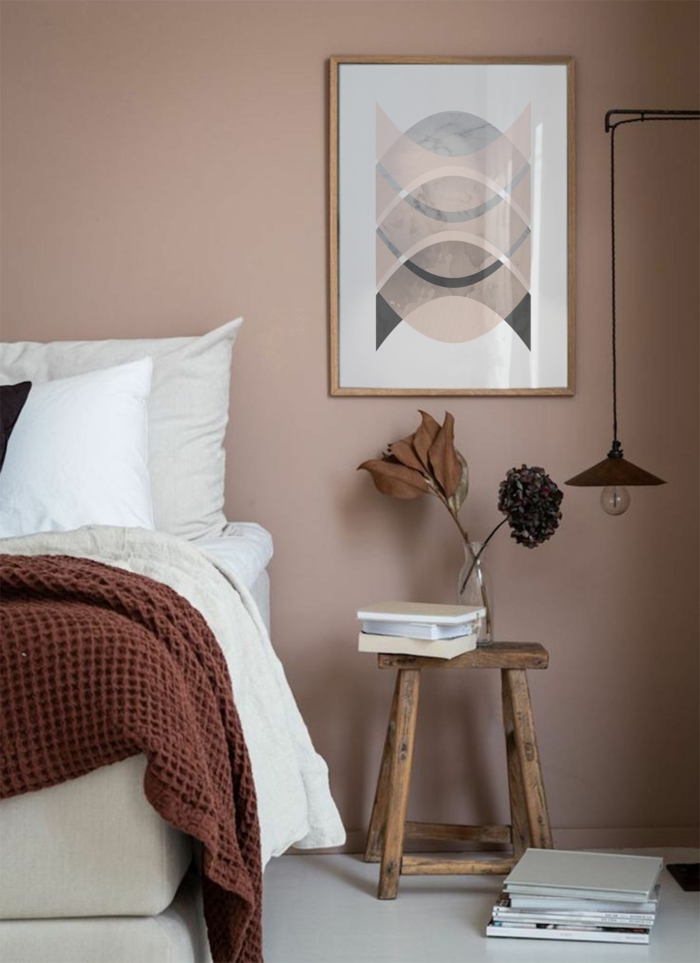 Schlafzimmer altrosa mit einem Bild in Pastelltöne, kleiner Tisch aus Holz mit Büchern und Blumen obendrauf, schwarze hängende Lampe, 