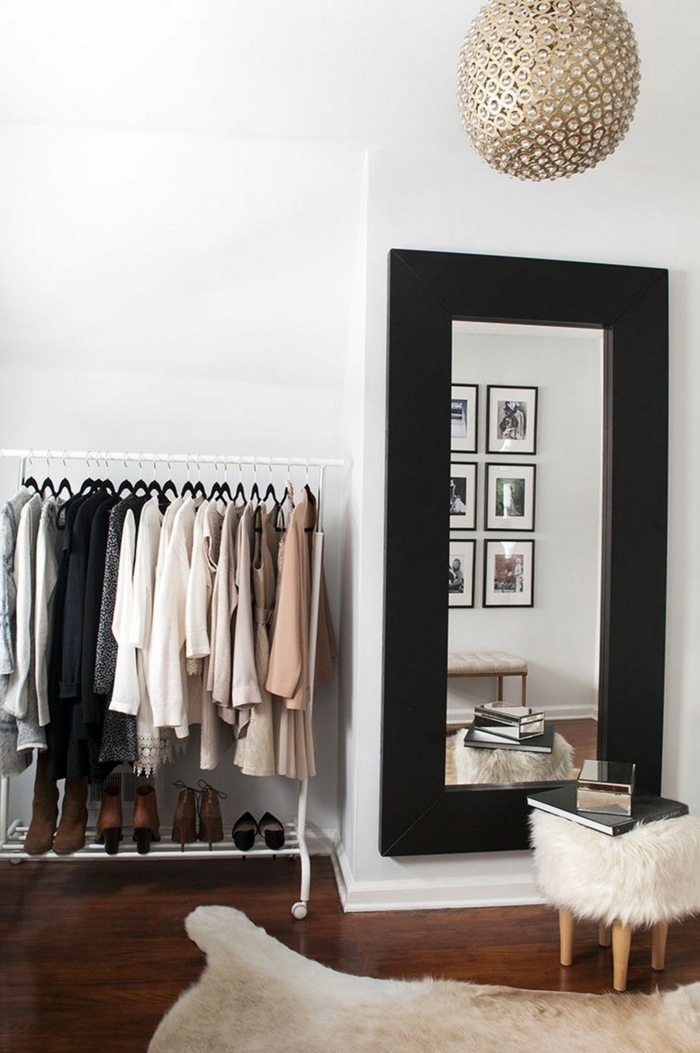 Ankleidezimmer kleiner Raum, Kleiderstange mit Klamotten, großer Spiegel mit schwarzem Rahmen, Teppich in weiß, Kronleuchter in goldener Farbe