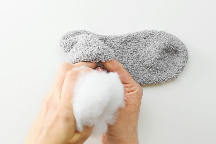 Anleitung zum basteln von Osterhasen aus Socken, Hand füllt Socke mit Stoff, Osterdeko selber machen, graue Socke