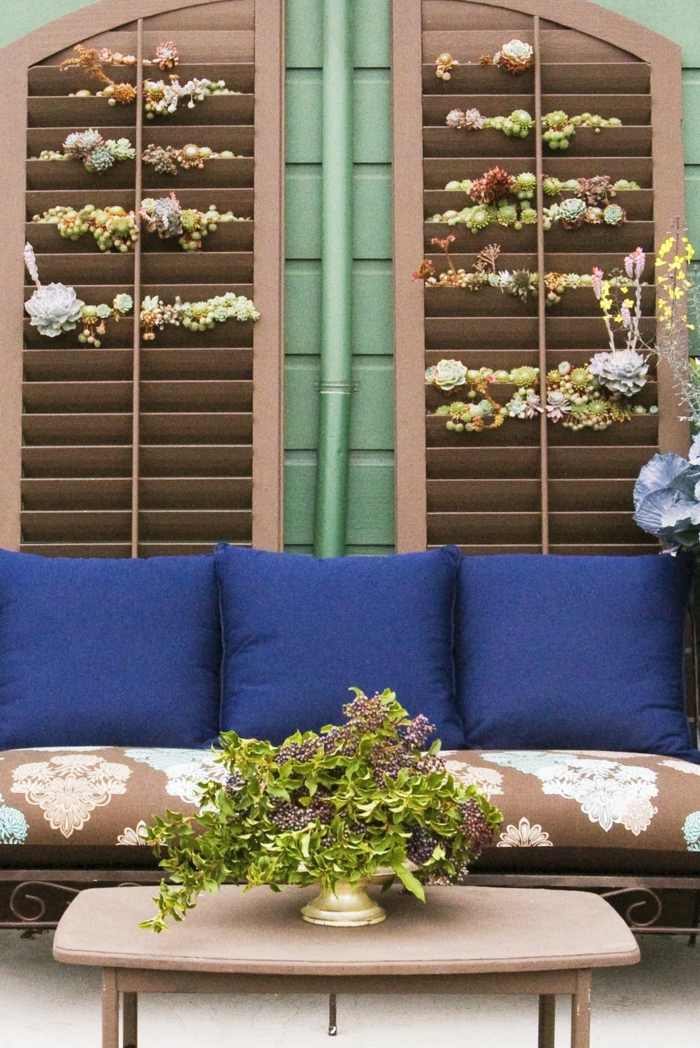 brauner Couch mit grellen blaufarbenen Kissen, Jalousien gefüllt mit Pflanzen, Ideen Gartengestaltung, grüne Pflanze auf einem Tisch