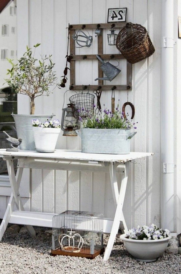 Ecke für Gartenzubehör mit einem recycletem Tisch in weiß, Boden aus Zierkies, Töpfe mit Blumen und einem kleinen Baum, Gartendeko aus Holz