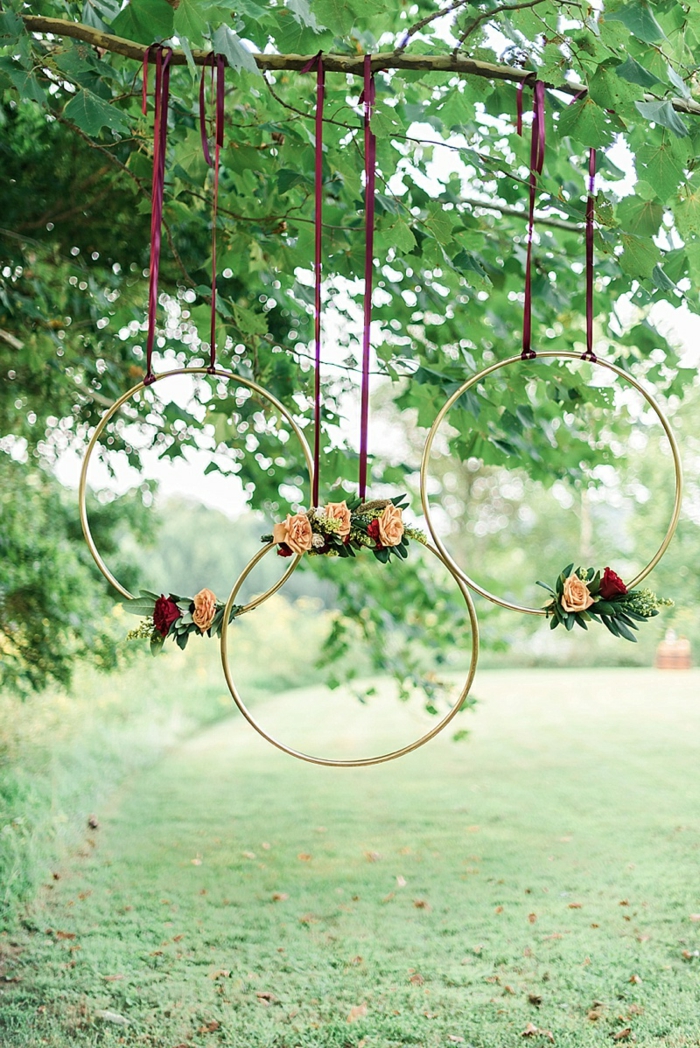 drei große Ringe aufgehängt auf einem Baumzweig und dekoriert mit rosa und rote Rosen, Gartendeko selber machen