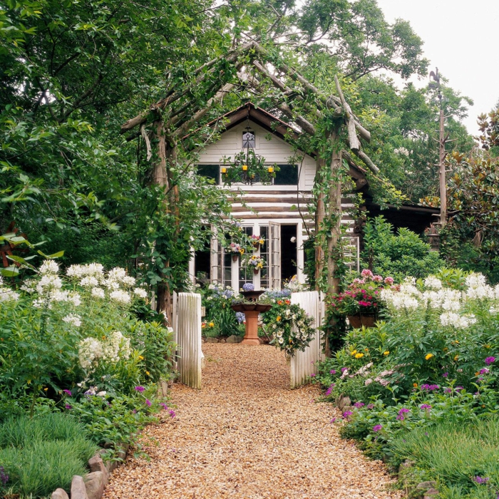 idyllisches Haus mit schönem grünen Garten, kleine Gartentür in weiß, Gartendeko aus Holz, Boden mit Zierkies