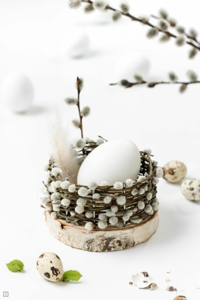 Osterdeko basteln aus Naturmaterialien, kleines Osterkörbchen aus Kätzchen Zweige auf einer Holzscheibe mit einem weißen Ei drin, Osterdeko selber machen