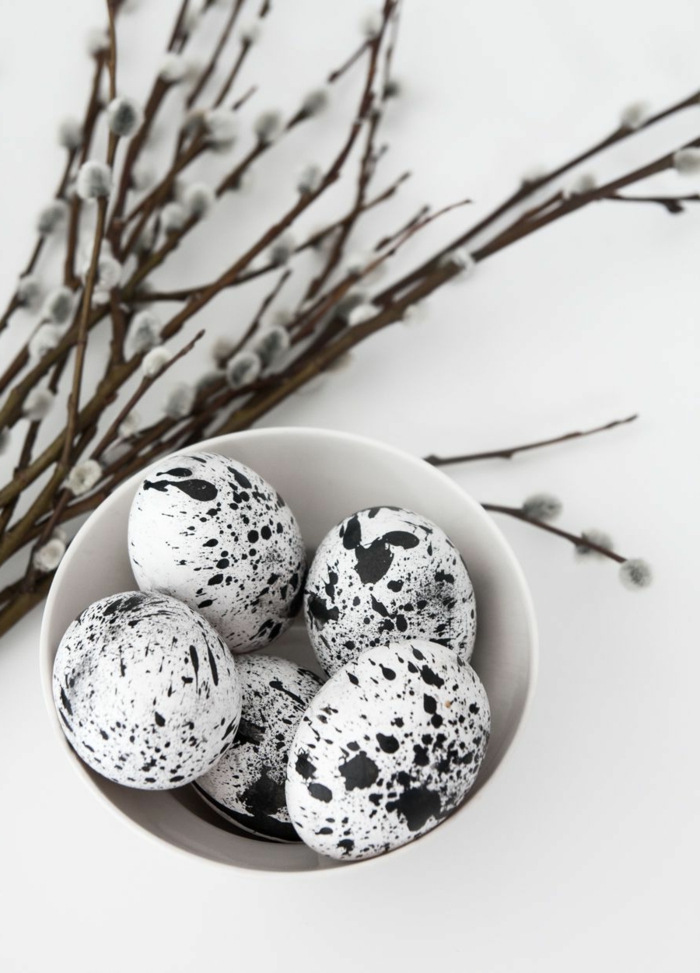 Bemalte kleine Ostereier in schwarz und weiß, Kätzchen Blumen im Hintergrund, Pinterest Osterdeko, minimalistische Dekoration