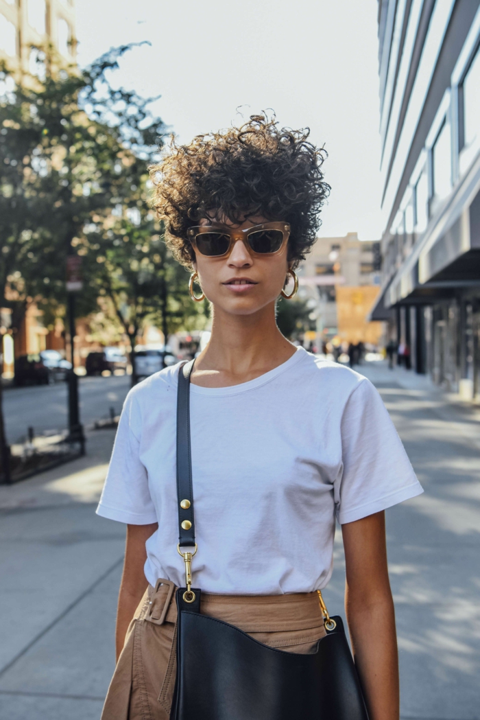 New York Street Style Inspiration, lockige Kurzhaarfrisuren, lässig gekleidete Frau, hellbraune Hosen mit Gürtel und weißes T-Shirt, schwarze Umhängetasche