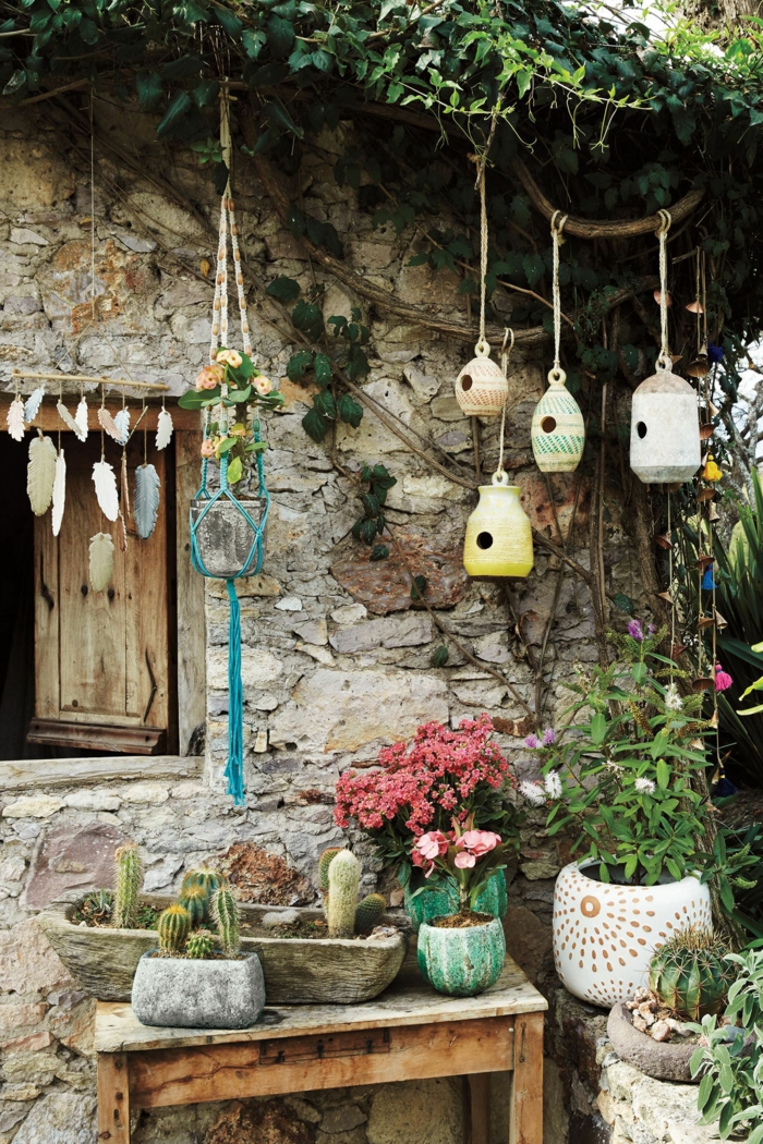 vier kleine selbstgemachte Vogelhäuser, viele Blumen und Kakteen, Wand eines Hauses aus Stein, Gartendeko selbstgemacht