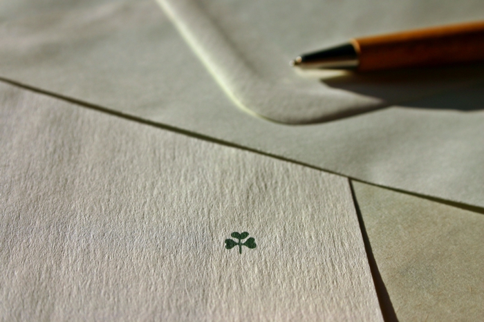 Nahaufnahme eines Briefumschlags, Kugelschreiber im Hintergrund, weißer Briefumschlag, dreiblättriger Kleeblatt