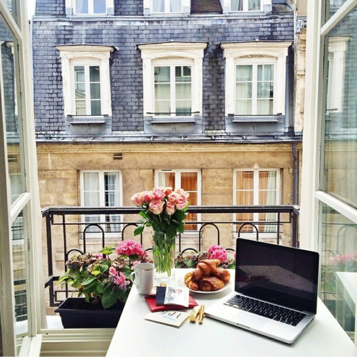 Laptop auf einem Tisch mit pinken Blumen, Ikea Balkon Ideen, offene Fenster, Croissant in einem Teller, 