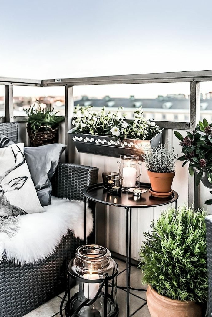 Möbel für kleinen Balkon, kleiner runder Tisch, graues Sofa mit Kissen und flauschiger Deke, grüne Pflanzen und Blumen