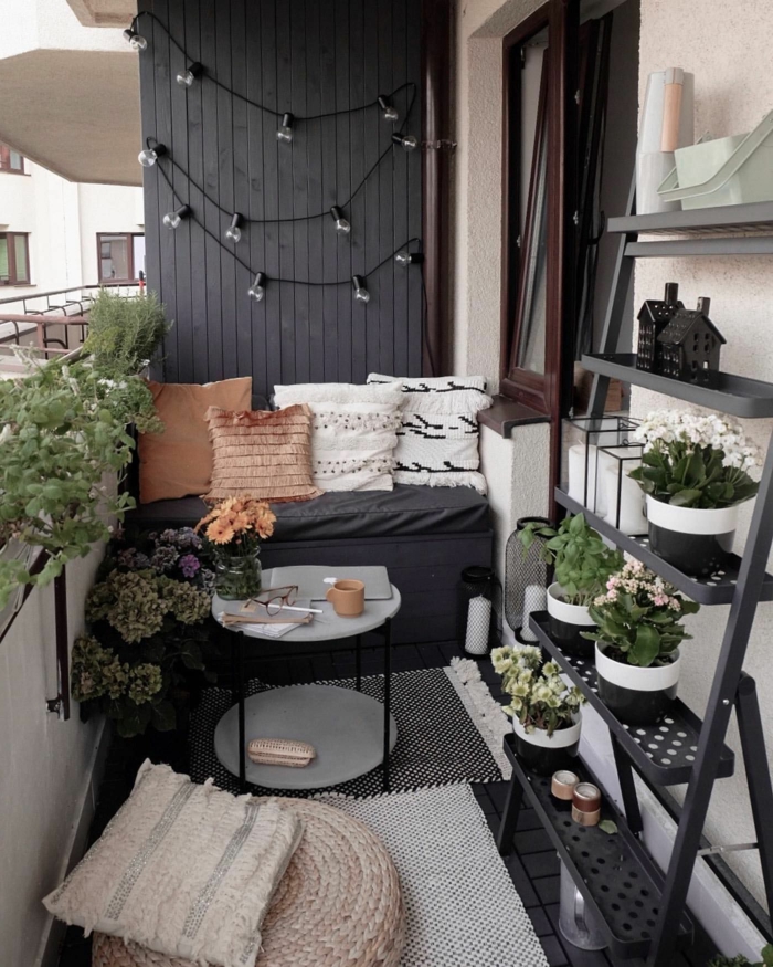 Balkon Lounge klein, schwarze Wand mit aufgehängten Hängeläuchter. Pflanzenständer mit vielen Pflanzen, kleiner grauer Sofa mit Kisse