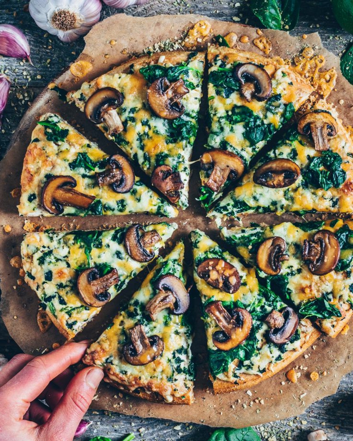aufgeschnittene Pizza mit Champignons Spinat und veganem Käse, Gemüse Rezepte vegan, Hand hält ein Stück der Pizza 