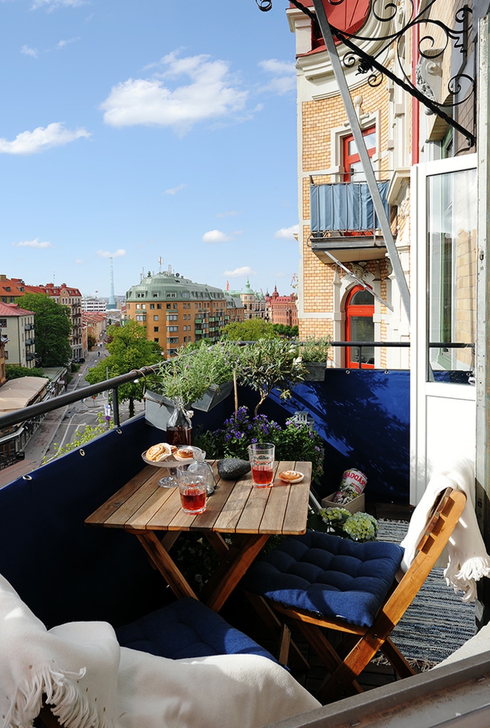 Terrasse mit Aussicht zur Straße, blaue Wand und Kissen, Balkon Lounge klein, kleiner dekorativer Baum