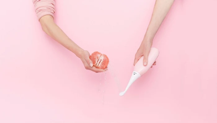 hand mit einer pinken dusche happypo, alternative zu dem klopapier in der coronavirus krise, hand mit einer grapefruit