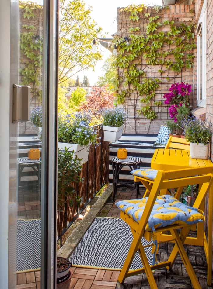 Farbige Einrichtung von Terrasse, gelber Tisch und gelbe Stühle, Kletterpflanzen und lila Blumen, Möbel für kleinen Balkon