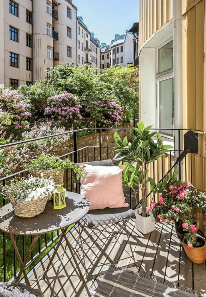 Dekoration mit vielen Blumen und Pflanzen, Möbel für kleinen Balkon, pinker Kissen auf grauem Stuhl