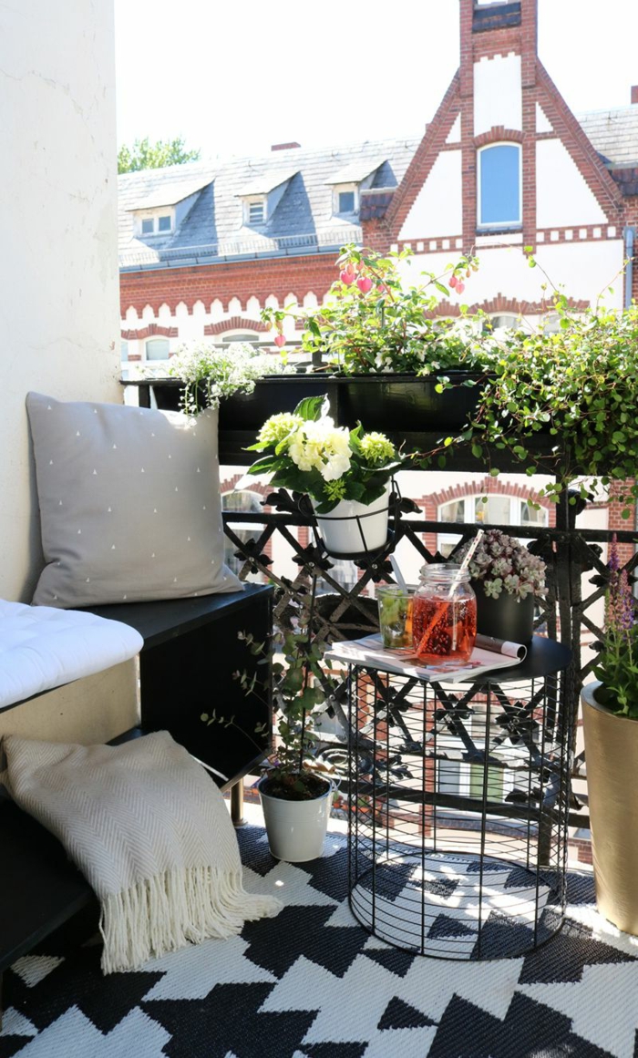 Wunderschöne weiße Blume in einem Topf, geometrischer Teppich in schwarze und weiße Farben, moderner Korbtisch. Balkon Lounge klein