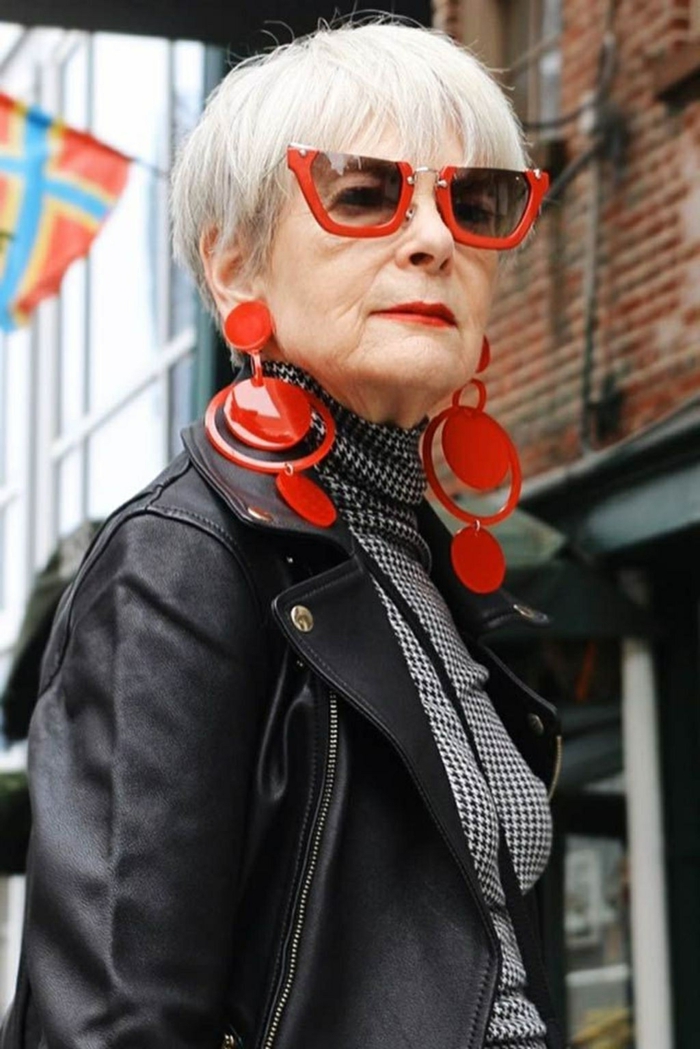 styisch gekleidete älter Dame, schwarze Lederjacke, große rote Ohrringe und Sonnenbrillen, gestufter bob für ältere frauen 