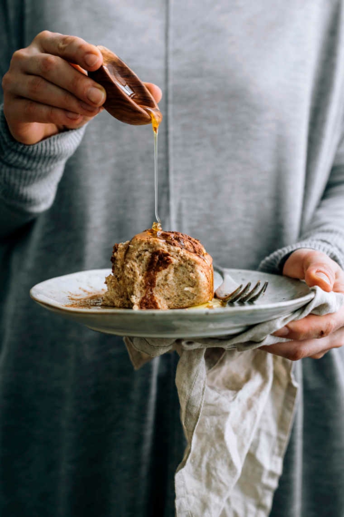 einfache vegane Rezepte zum backen, Zimtschnecken mit Nüssen, Hand gießt Ahornsirup auf einem Keks, Frau in graue Bluse