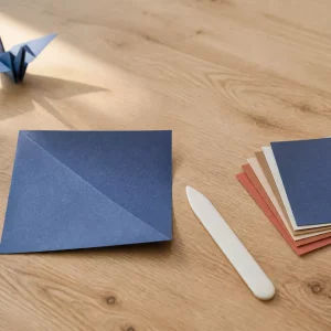 Origami Anleitung: halb gefaltetes blaues Papier auf hellem Holztisch