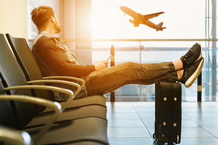 lässig angezogener Mann wartet auf einem Flughafen, kleiner handgepäck koffer, fliegender Flugzeug, das perfekte reisegepäck